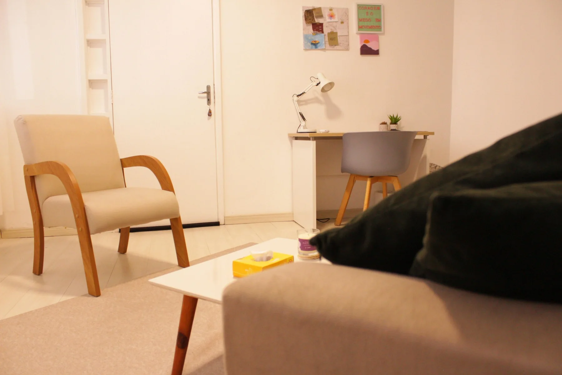 Consultório visto a partir do sofá, com poltrona e mesa de trabalho